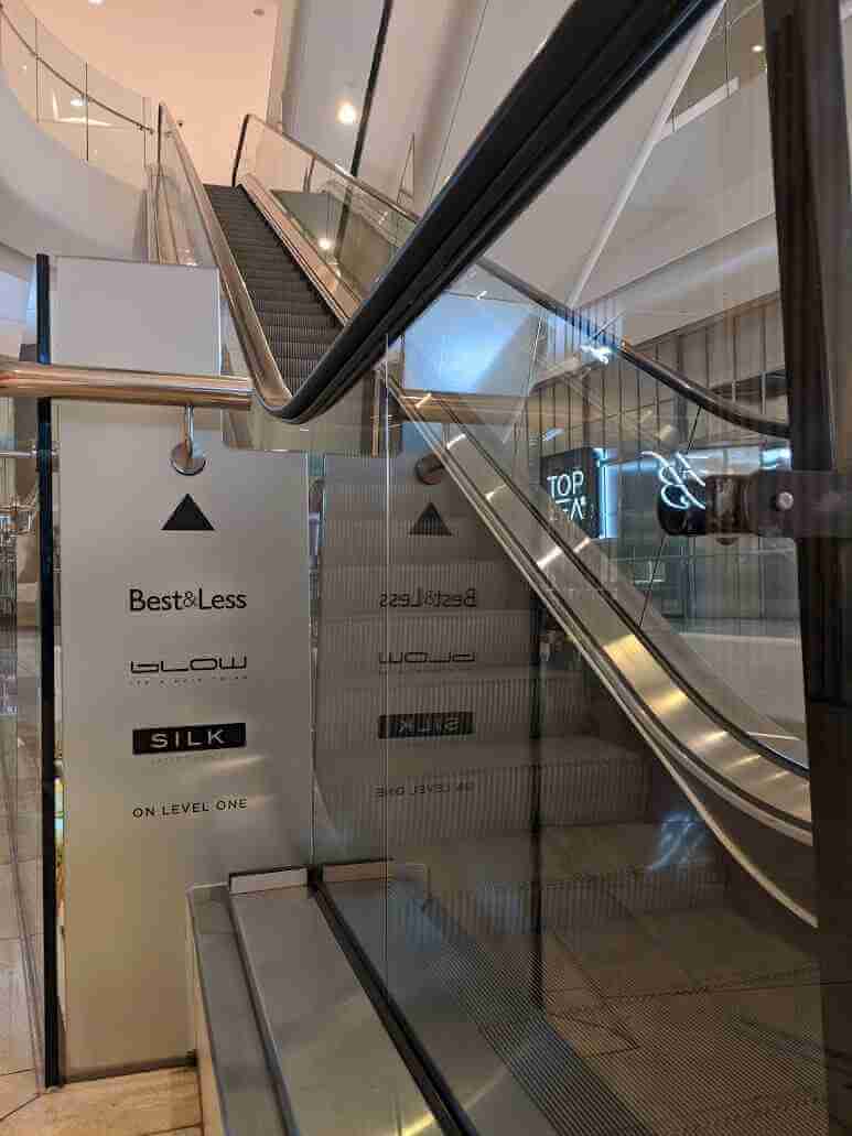 Glass panel signage listing building directories and wayfinding information near escalator