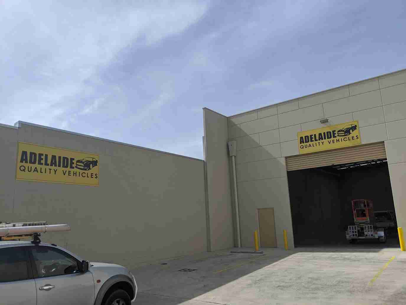 Large yellow warehouse signage for Adelaide Quality Vehicles dealership mounted on facade